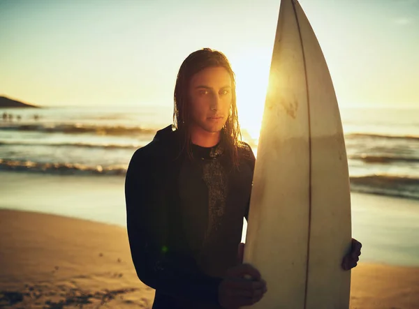 Ser surfista está simplemente en mi sangre. Retrato de un joven de pie con una tabla de surf en la playa. —  Fotos de Stock