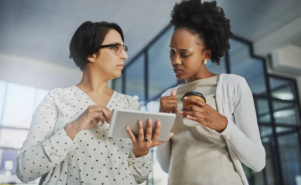 Kijkt u eens goed. Low angle shot van twee zakenvrouwen op zoek naar een tablet in het kantoor. — Stockfoto