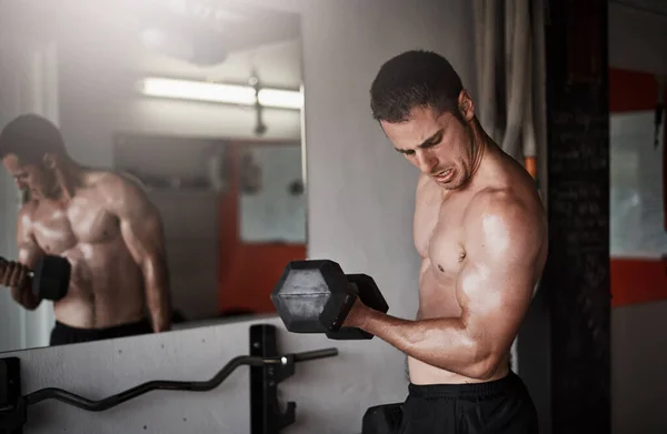 Centrándose en sus bíceps. Cortado tiro de un joven guapo y musculoso haciendo ejercicio con una mancuerna en el gimnasio. — Foto de Stock