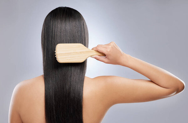 My is is stronger and healthier. Shot of a young woman brushing her hair while standing against a grey background.