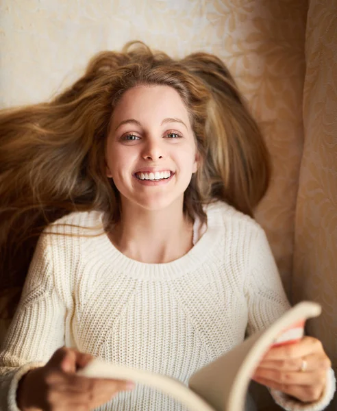 Lezen is mijn favoriete hobby. Portret van een aantrekkelijke jonge vrouw die een boek leest terwijl ze thuis op de bank ligt. — Stockfoto