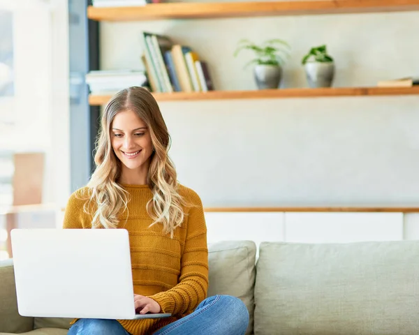 Haar blog bijwerken. Foto van een aantrekkelijke jonge vrouw met behulp van haar laptop tijdens het zitten op de bank thuis. — Stockfoto