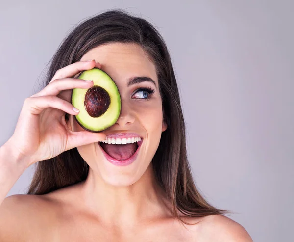 Pomůže to tvé pokožce zářit. Studio záběr atraktivní mladé ženy, která si zakrývá oko avokádem proti fialovému pozadí. — Stock fotografie