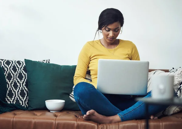 Komfort steht immer an erster Stelle. Aufnahme einer attraktiven jungen Frau, die allein zu Hause sitzt und ihren Laptop benutzt. — Stockfoto