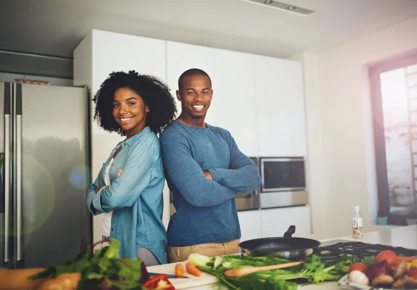 Fazemos a melhor equipa. Retrato de um jovem casal alegre em pé junto sobre uma mesa cheia de ingredientes que eles estão prestes a usar para cozinhar na cozinha em casa. — Fotografia de Stock