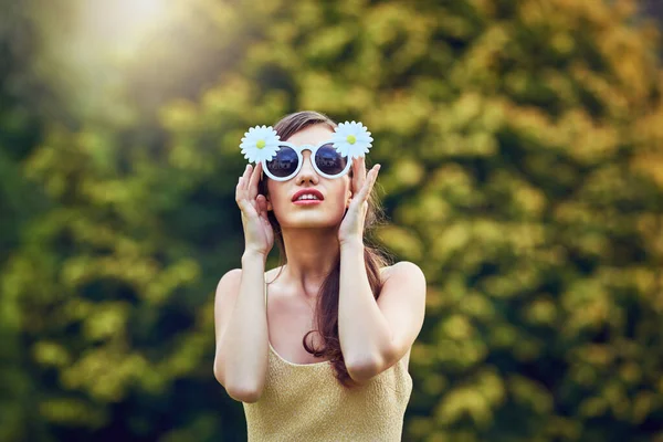 Сонце її любить. Портрет привабливої молодої жінки в сонцезахисних окулярах, тримаючи їх і стоячи зовні в природі протягом дня . — стокове фото