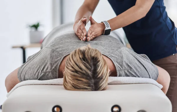 Votre dos a besoin de tout le soulagement qu'il peut obtenir. Prise de vue d'une femme mature allongée face contre terre et se faisant masser le dos par un physiothérapeute dans une clinique. — Photo