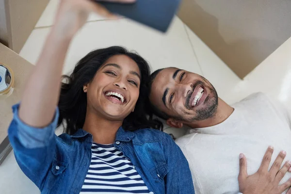 Documentar o início de um novo capítulo. Tiro de um jovem casal feliz tirando uma selfie enquanto se mudam para sua nova casa juntos. — Fotografia de Stock