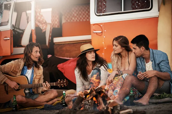 Szczęście to spędzanie czasu z przyjaciółmi. Przycięte ujęcie grupy przyjaciół siedzącej przy ognisku na plaży. — Zdjęcie stockowe
