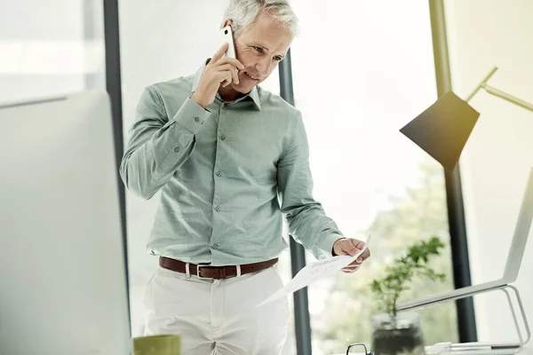 Hablando del contrato. Fotografía de un hombre de negocios maduro hablando por teléfono mientras trabajaba de pie en su escritorio en una oficina. —  Fotos de Stock