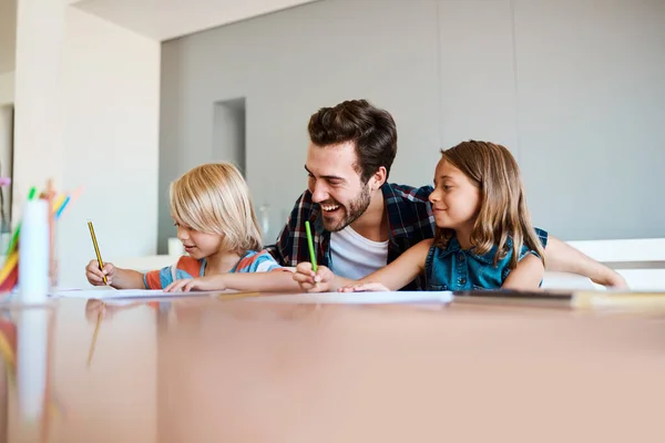 Les encanta cuando su papá está cerca. Fotografía de un padre joven ayudando a sus dos hijos pequeños con sus deberes en casa. — Foto de Stock