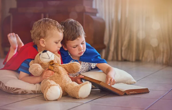 俺の言う通りにしてくれ。家の床に横になっている間に本で遊んでいる2人の男の子のショット. — ストック写真