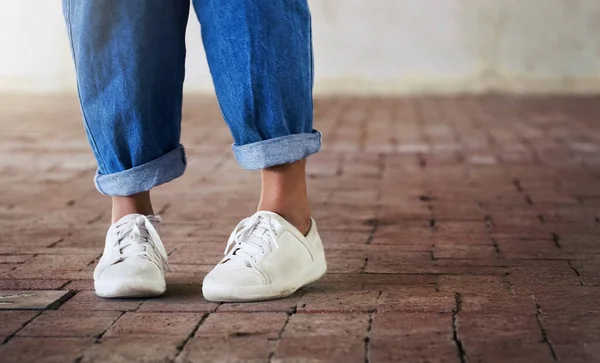 Schuhe an, tanzen lassen. Schnappschuss einer unkenntlichen Person, die auf einem Ziegelboden steht, während sie weiße Turnschuhe und blaue Jeans trägt. — Stockfoto