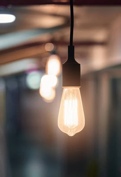 Es braucht nur eine brillante Idee. Schuss einer Glühbirne, die abends in einem leeren Büro von der Decke hängt. — Stockfoto