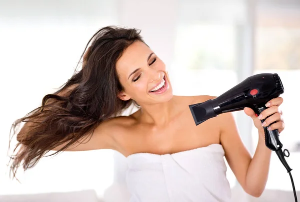 Starat se o její vlasy. Krásná žena se usmívá, zatímco si suší vlasy fénem. — Stock fotografie