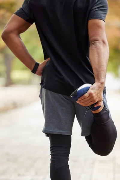 Strek het uit voordat je begint. Achteraanzicht van een onherkenbare man die zijn benen strekt terwijl hij buiten traint. — Stockfoto