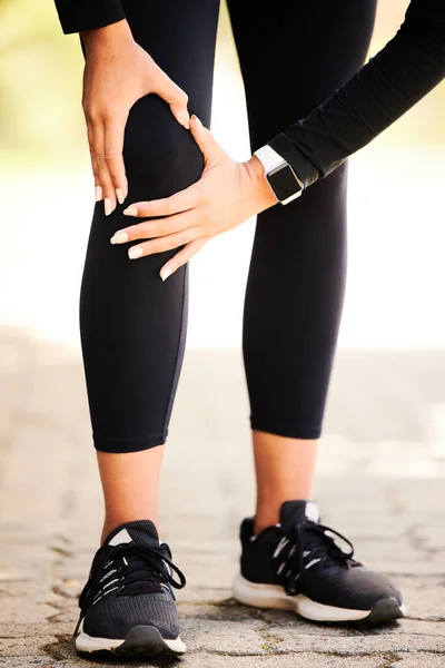 Shes having a little trouble with her knee. Cropped shot of an unrecognizable and athletic woman holding her knee in discomfort while standing outdoors. — Stock Photo, Image