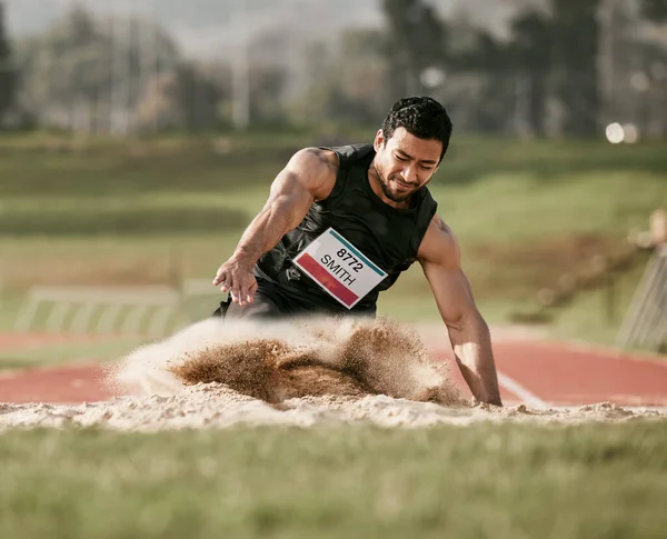 Stick the landing. Full length shot of a handsome young man competing in a long jump event outside. — Stock Photo, Image