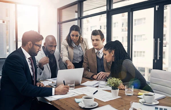 O trabalho em equipe é o último impulsionador de produtividade. Tiro de um grupo de jovens empresários usando um laptop juntos durante uma reunião em um escritório moderno. — Fotografia de Stock
