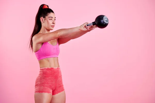 Varje utmaning är menad att förändra dig. Studio skott av en sportig ung kvinna som tränar med en kettlebell mot en rosa bakgrund. — Stockfoto