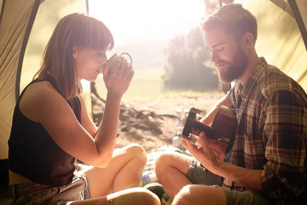 E 'ora del caffe' al campo. Girato di un giovane che suona la chitarra alla sua ragazza in una tenda. — Foto Stock