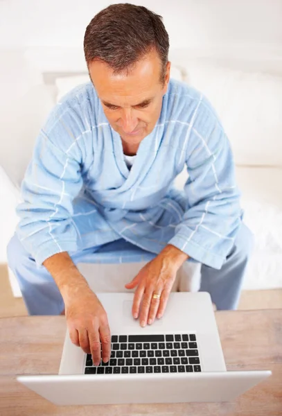Ένας ηλικιωμένος με μπουρνούζι που δουλεύει σε ένα λάπτοπ στο σπίτι. Άνοδος άποψη ενός ηλικιωμένου συνταξιούχου που εργάζεται σε ένα φορητό υπολογιστή στο σπίτι. — Φωτογραφία Αρχείου