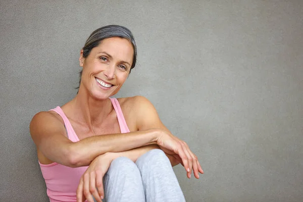 Prowadzić zdrowy tryb życia. Portret atrakcyjnej dojrzałej kobiety w stroju gimnastycznym siedzącej na szarej ścianie. — Zdjęcie stockowe