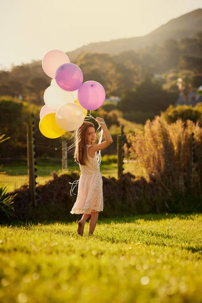 Es una cumpleañera afortunada. Retrato de una linda niña sosteniendo un gran montón de globos mientras camina afuera. — Foto de Stock