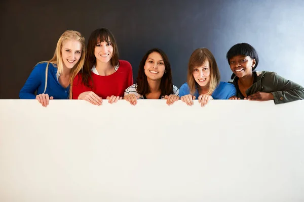 Platzieren Sie Ihre Nachricht hier. Aufnahme einer Gruppe von Frauen mit einem leeren Schild vor dunklem Hintergrund. — Stockfoto