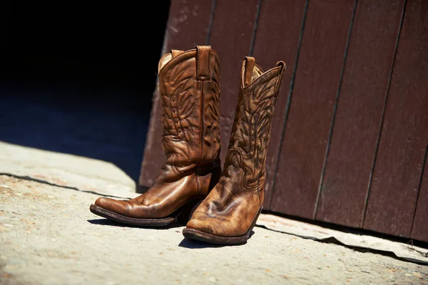 Worn in by hard work. Shot of a pair of cowboy boots outside a barn. — Stock Photo, Image