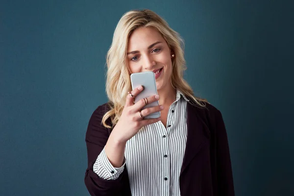 No puedes evitar que lleve su negocio a nuevas alturas. Captura de estudio de una hermosa joven empresaria usando un teléfono celular sobre un fondo azul. —  Fotos de Stock