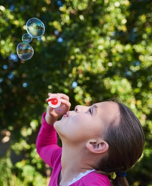 Nothing says childhood like blowing bubbles. Shot of a cute young girl blowing bubbles outside. — ストック写真