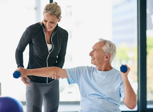 C'est une professionnelle si amicale. Plan recadré d'un homme âgé heureux travaillant avec des poids avec l'aide d'un physiothérapeute. — Photo