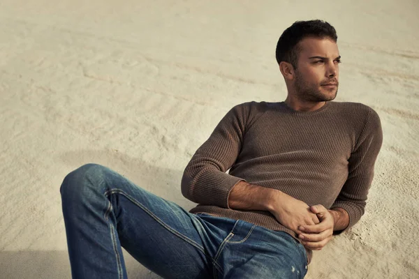 Se ve elegante en el desierto. Un guapo modelo masculino reclinado en la arena del desierto con ropa de moda. —  Fotos de Stock