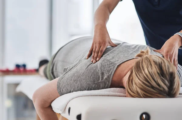 Está aquí para quitarte la carga de la espalda. Inyección de una mujer madura acostada boca abajo y recibiendo un masaje de espalda por un fisioterapeuta en una clínica. — Foto de Stock