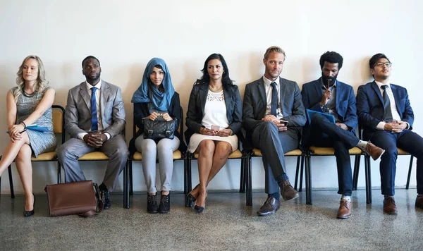 Esperando causar una impresión memorable. Fotografía de un grupo de empresarios bien vestidos sentados en fila mientras esperan ser entrevistados. — Foto de Stock
