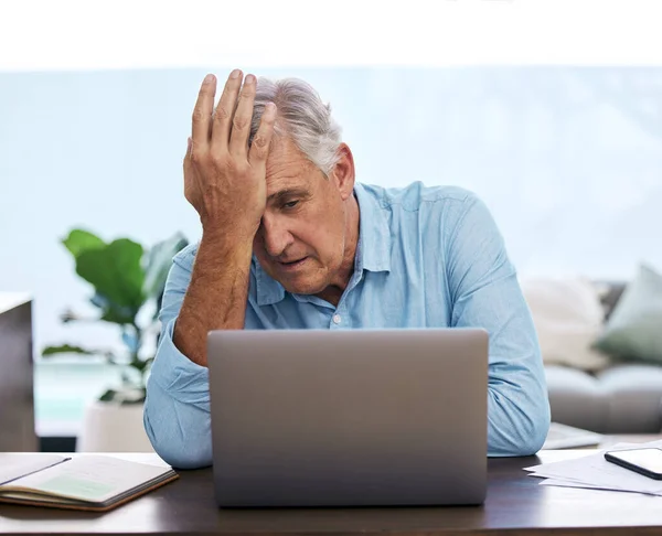 Oh no, not again. Shot of a mature man sitting alone and feeling stressed while using his laptop to work from home. — ストック写真