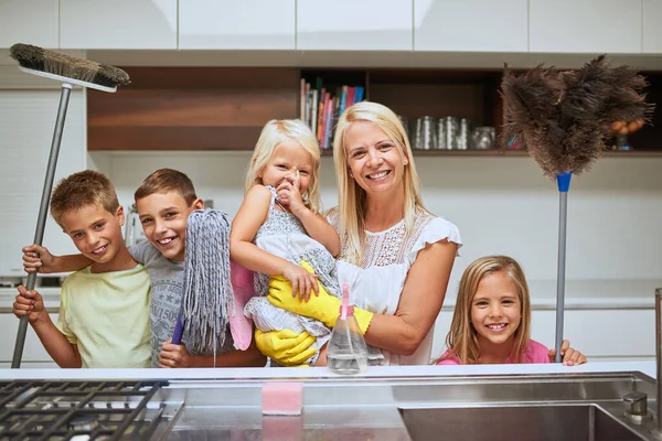 Moms got many helpers to keep their home sparkling clean. Portrait of a mother and her kids doing chores together at home. — Stock Photo, Image