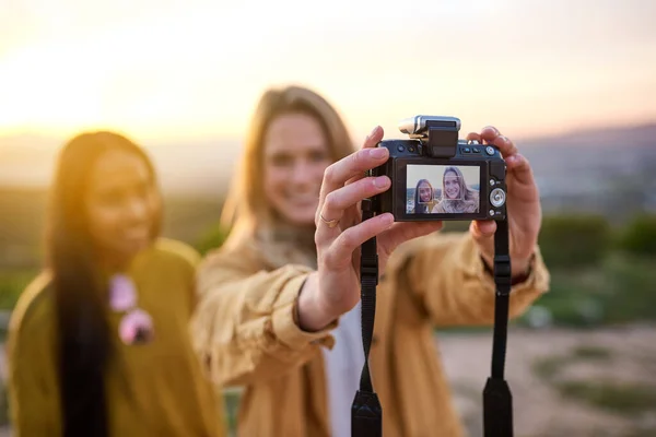 O cenário perfeito para uma selfie. Tiro de dois amigos tirando uma selfie com uma câmera digital enquanto estava do lado de fora. — Fotografia de Stock
