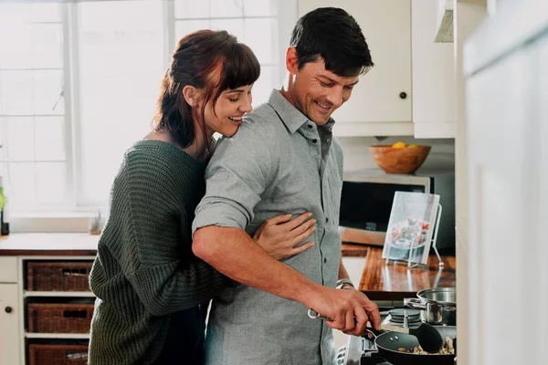 A comida sabe melhor quando feita com amor. Tiros de um homem cozinhando ao ser abraçado por sua esposa em casa. — Fotografia de Stock
