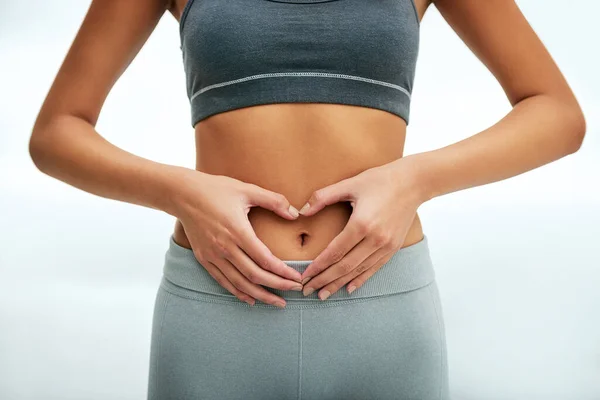 Ama tu cuerpo y te amará de nuevo. Foto recortada de una mujer formando una forma de corazón en su estómago. —  Fotos de Stock