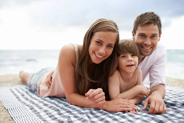 Наслаждаюсь расслабляющим отдыхом. Портрет счастливой молодой семьи, лежащей на пляжном одеяле. — стоковое фото