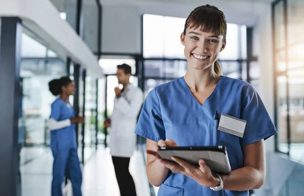 Modern healthcare requires modern technology. Shot of a young doctor using a digital tablet in a hospital with her colleagues in the background. — Stock Photo, Image