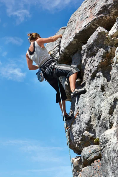 A adrenalina está a levá-la ao cume. Uma jovem mulher escalando um rosto de rocha enquanto emoldurado contra um céu azul. — Fotografia de Stock