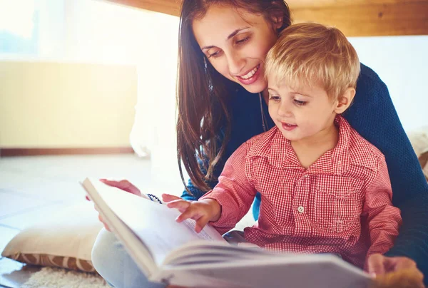 Znalezienie radości w nowych opowieściach. Zdjęcie matki czytającej książkę ze swoim synkiem w domu.. — Zdjęcie stockowe
