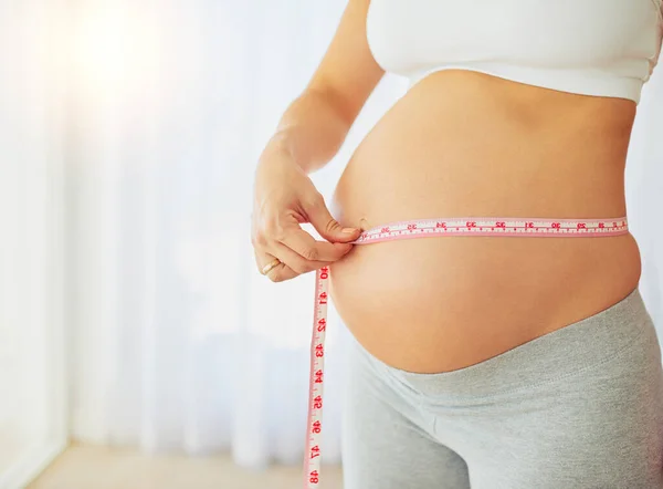 Tracking pregnancy milestones with regular measurements. Cropped shot of a pregnant woman measuring her belly at home. — Stock Photo, Image