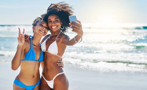 Reste sur la plage. Prise de vue de deux jeunes femmes prenant selfies ensemble à la plage. — Photo