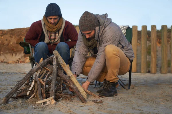 Lasst uns dies ein loderndes Beispiel sein. Zwei junge Männer bauen Feuer am Strand. — Stockfoto