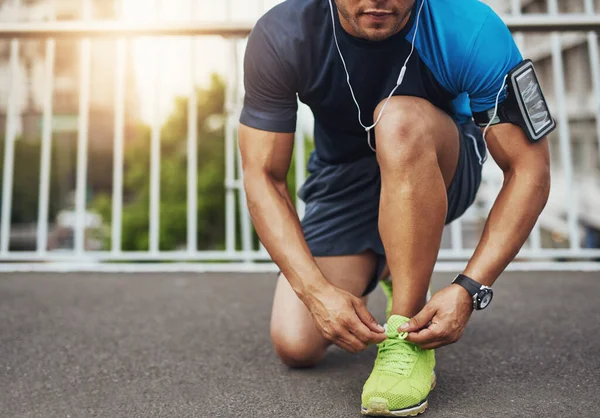 Vive per la sua corsa quotidiana. Girato di un giovane uomo legandosi i lacci delle scarpe prima di una corsa. — Foto Stock