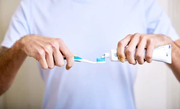 दिवसातून दोनदा ब्रश केल्याने पोकळी दूर राहते. त्याच्या टूथब्रशवर टूथपेस्ट लागू करणार्या माणसाचा शॉट . — स्टॉक फोटो, इमेज